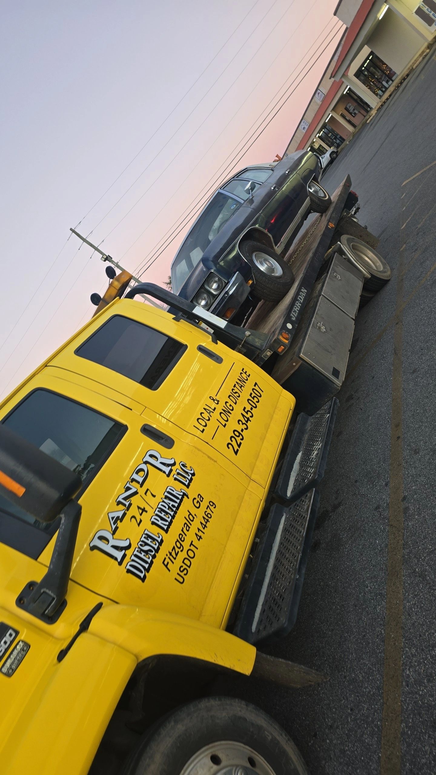 Yellow tow truck from R&R Diesel Repair carrying a damaged truck